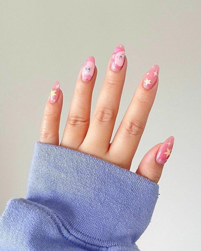 Hand with pink nail art ideas featuring cartoon faces and star designs, showcasing creative tiny little nail artworks.