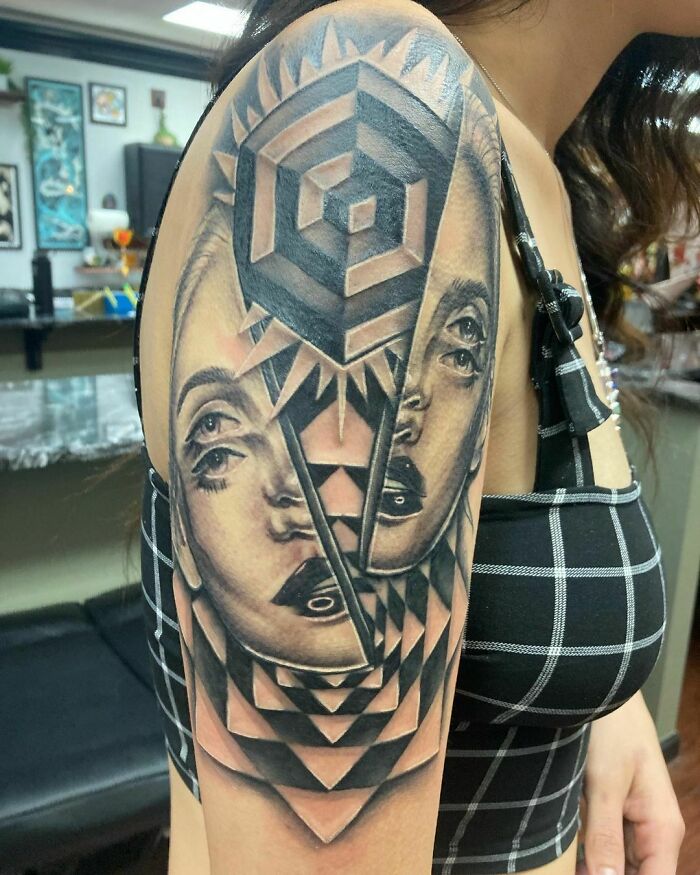 Optical illusion tattoo on a woman's upper arm, featuring a geometric and dual face design.