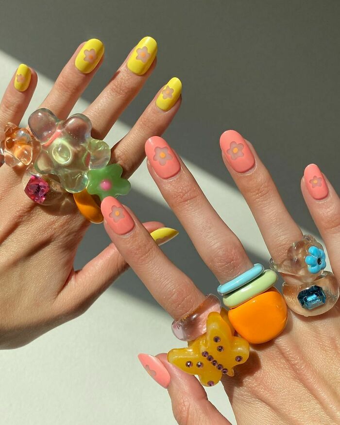 Colorful nail art with flower designs and bold, chunky rings.