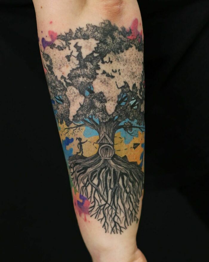 Optical illusion tattoo of a tree with intricate roots and branches blending into a colorful background on an arm.