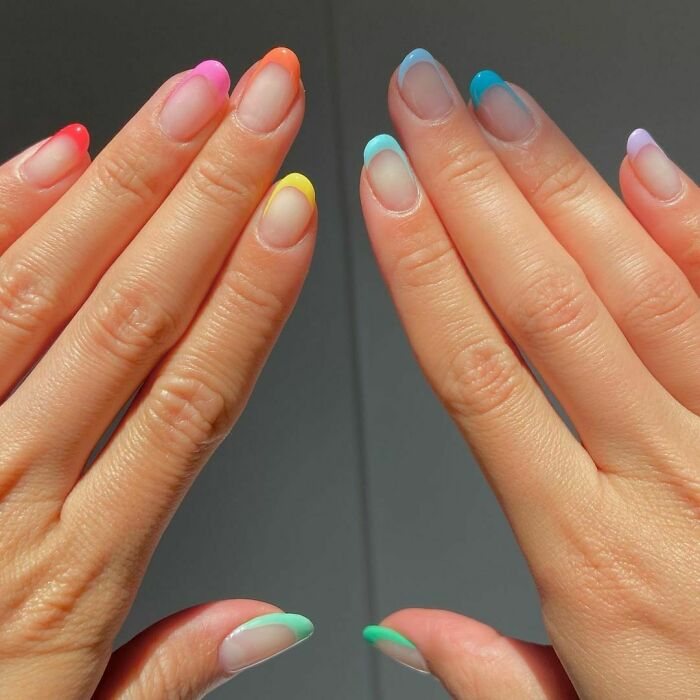 Close-up of hands with colorful nail art ideas featuring pastel French tips on natural nails.