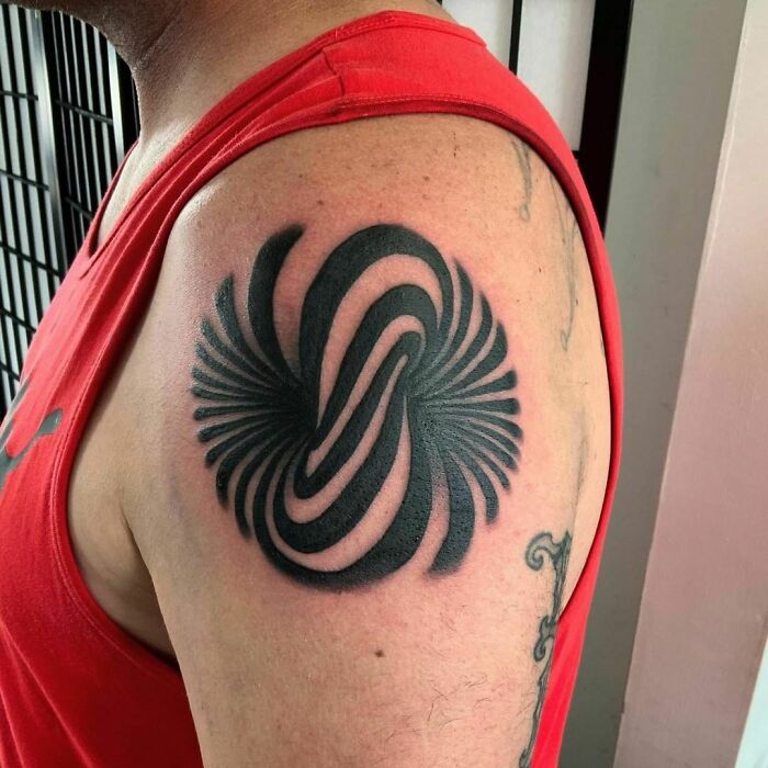 Optical illusion tattoo of swirling patterns on a person's upper arm in a red tank top.