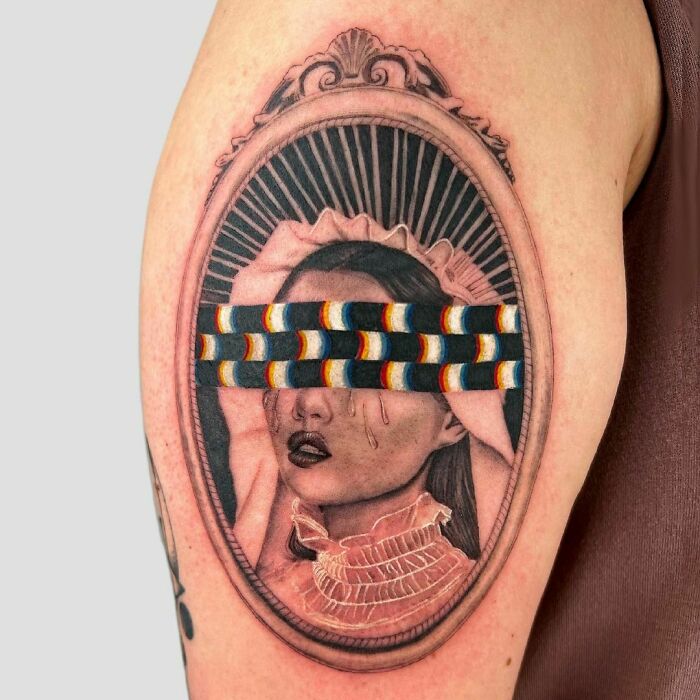 Optical illusion tattoo of a portrait with a colorful patterned band across the eyes on an arm.
