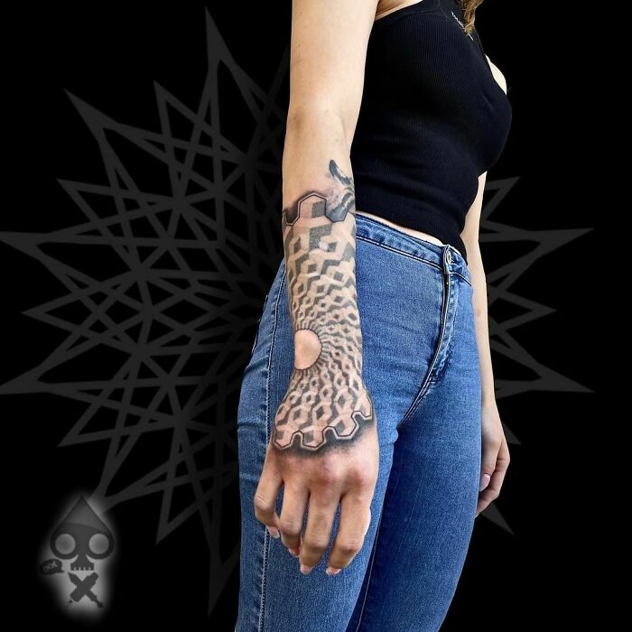 Person with an optical illusion tattoo on their arm, featuring mind-bending geometric designs.