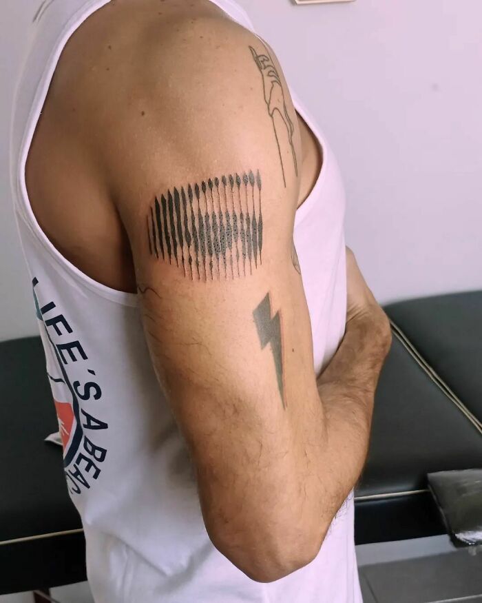 Arm with optical illusion tattoo featuring an eye design next to a bolt, showcasing mind-bending art.
