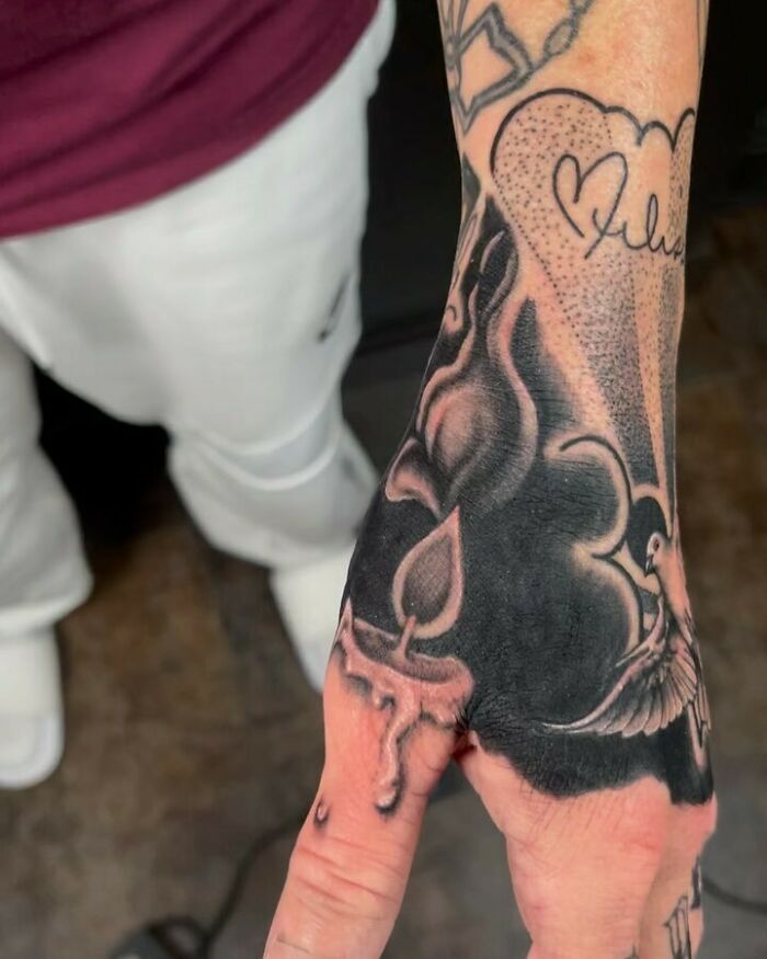 Intricate optical illusion tattoo on hand with candle, rose, and bird design.