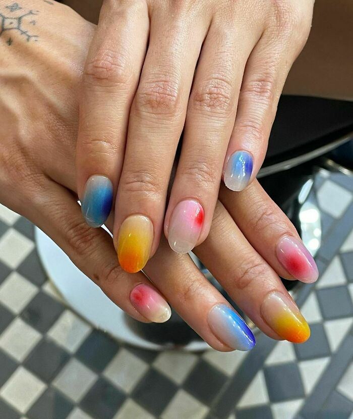 Close-up of hands with colorful nail art designs blending blue, yellow, red, and pink shades showcasing creative nail art ideas.