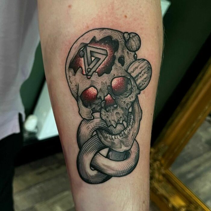 Tattoo of a skull with a geometric design and an intertwined shape, showcasing an optical illusion effect.