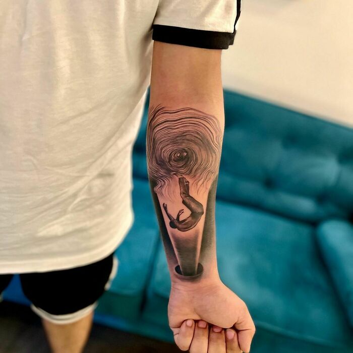 Forearm with an optical illusion tattoo of a person falling into a vortex.
