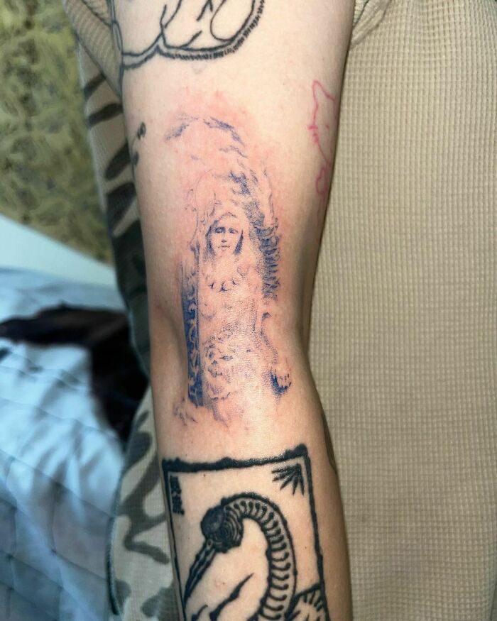 Arm with faded tattoos, including a detailed figure and a black design, showcasing less attractive tattoo choices.