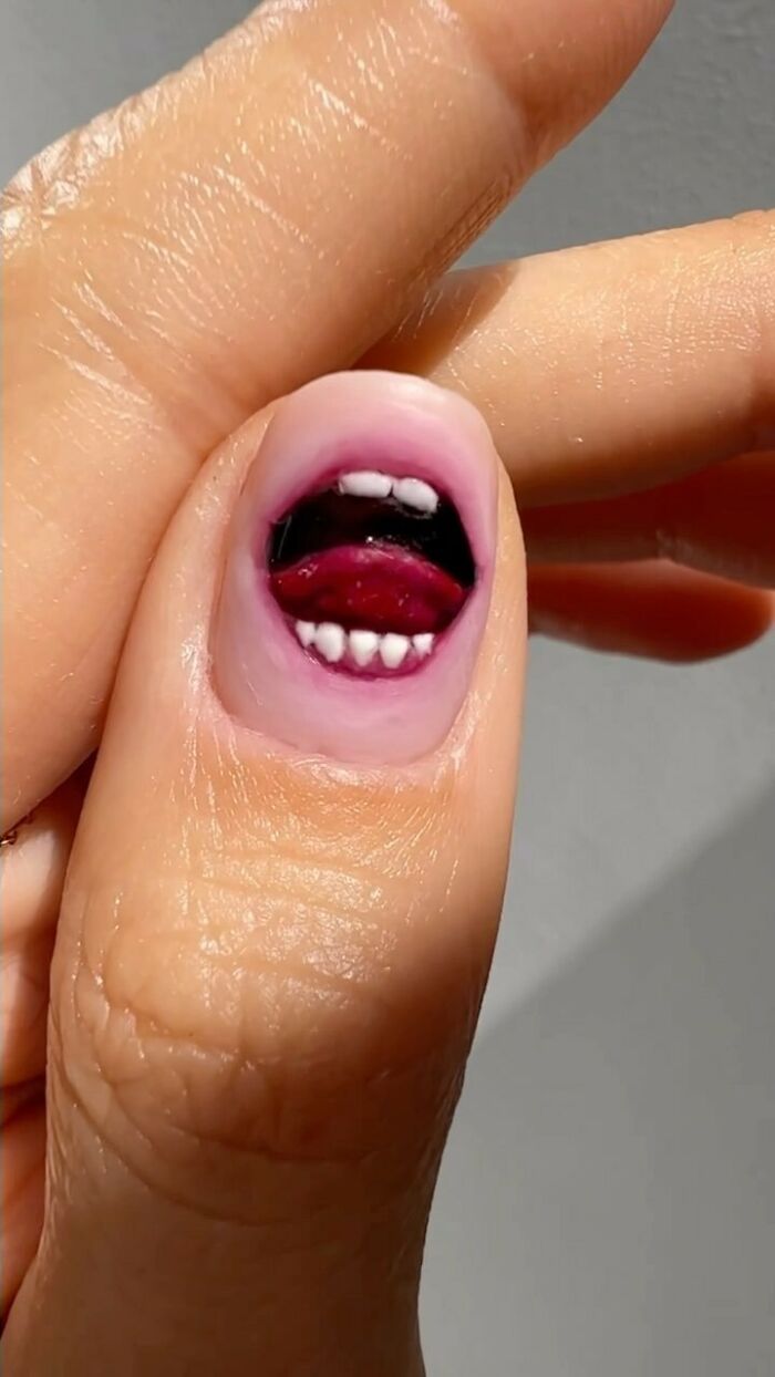 Creative nail art design featuring a realistic mouth painted on a thumb.