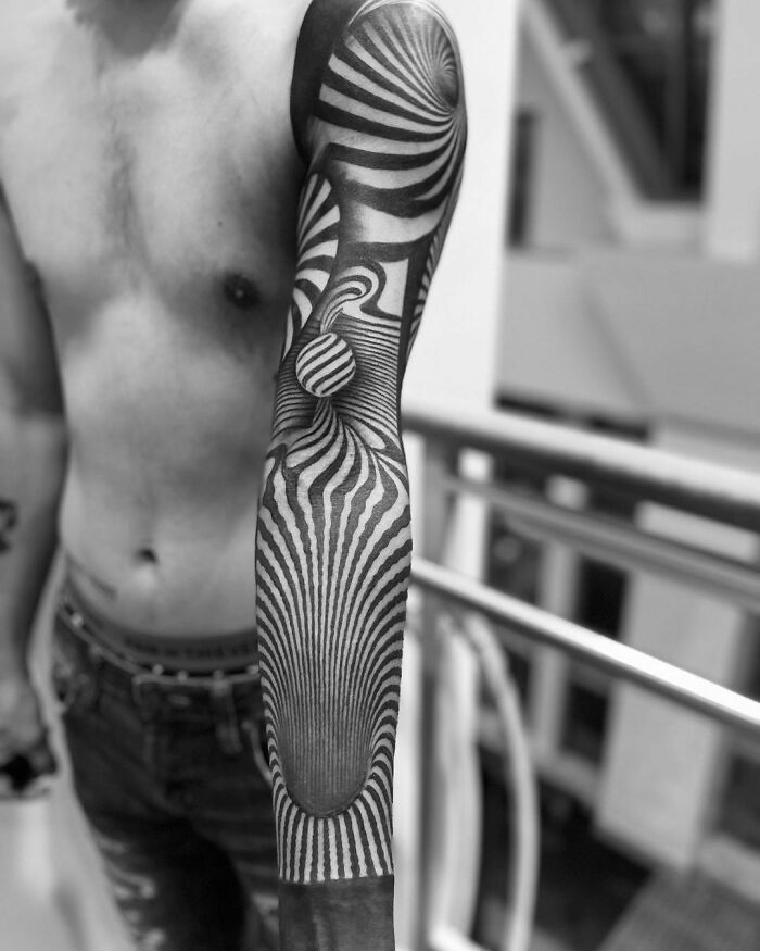 Man with intricate optical illusion tattoo sleeve, featuring swirling patterns and 3D effects.