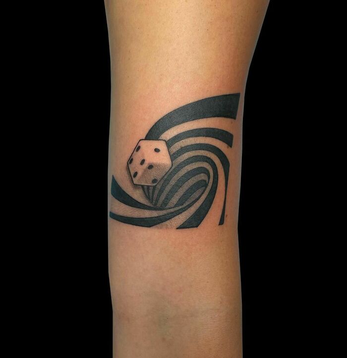 Optical illusion tattoo of a dice with swirling black and gray patterns on skin.