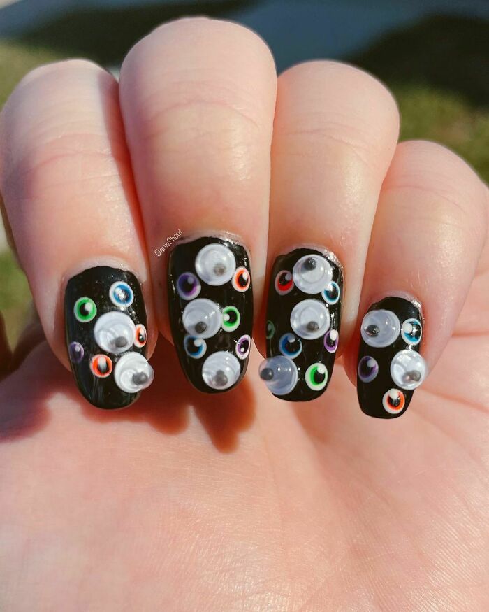 Colorful nail art with 3D eyes on black polish.