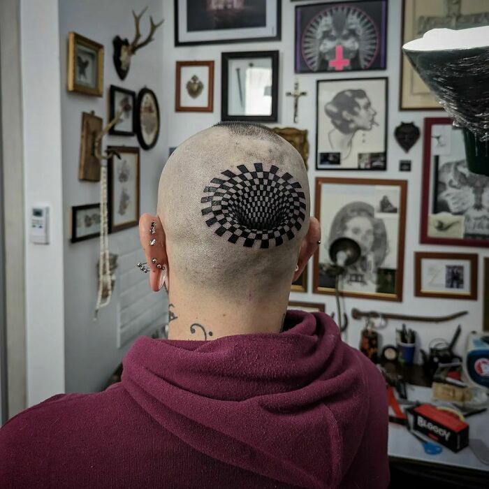 Optical illusion tattoo on the back of a shaved head in an art-filled room.