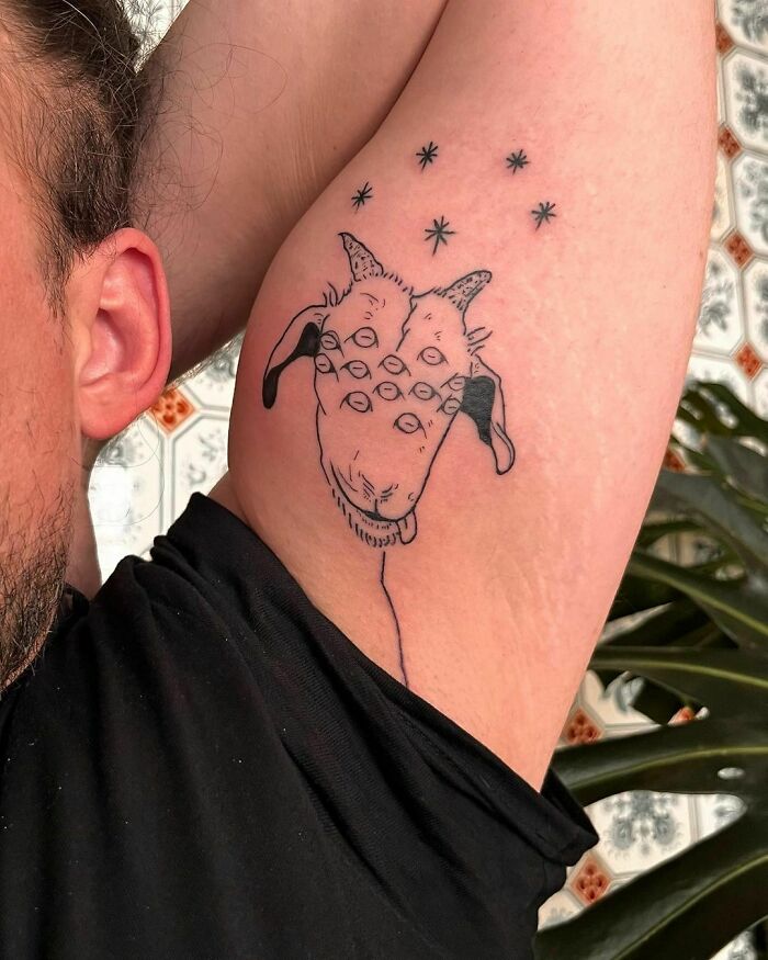 Funny tattoo of a goat with multiple eyes on an arm, stars above.