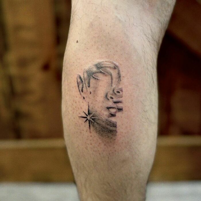 Optical illusion tattoo on calf, featuring face and star design, creating a mind-bending effect.