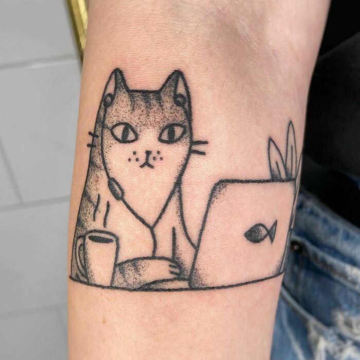 Funny working cat tattoo with headset, coffee cup, and laptop on arm.