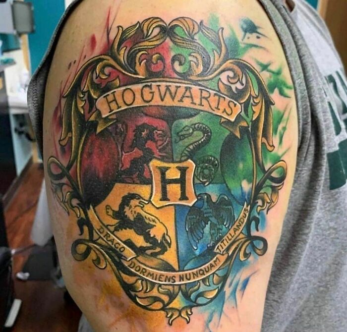 Colorful Harry Potter tattoo of the Hogwarts crest on an arm, featuring house emblems and intricate details.