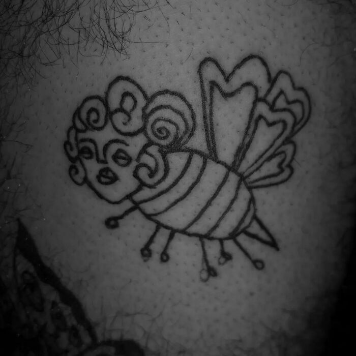 Funny tattoo of a human-faced bee with curly hair and striped body.