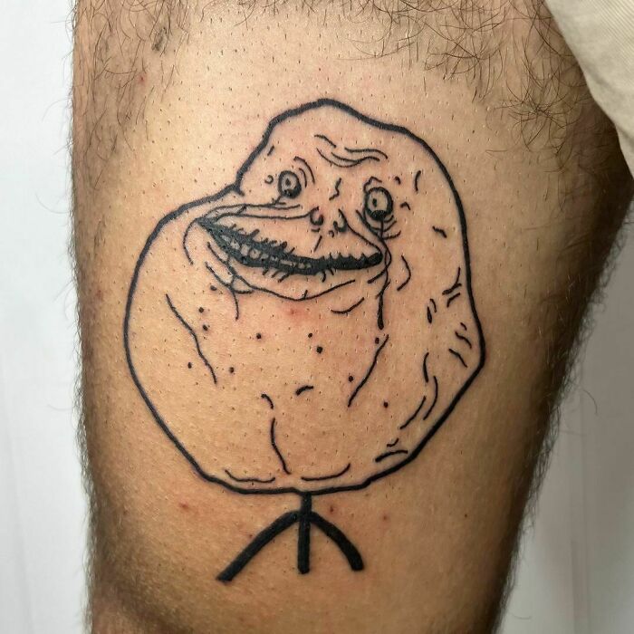 Funny tattoo of a meme face with a simplistic stick figure body, designed to bring a smile.