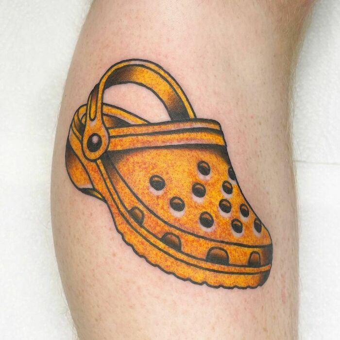 Funny tattoo of a yellow Croc shoe on a person's leg.