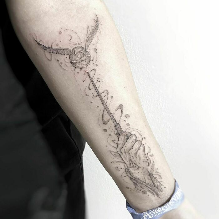 Harry Potter tattoo of a wand and Golden Snitch on a forearm, showcasing wizarding world art.