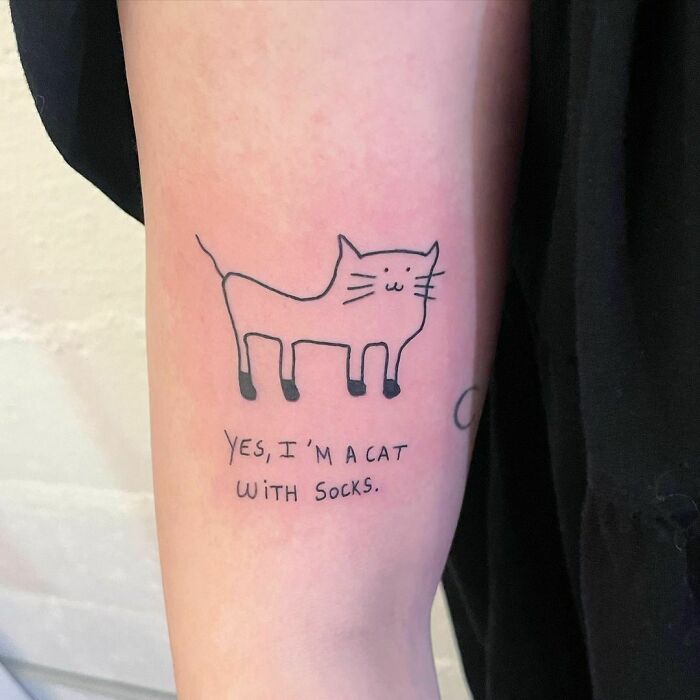 Funny tattoo of a simple cat drawing with text, "Yes, I'm a cat with socks," on an arm.