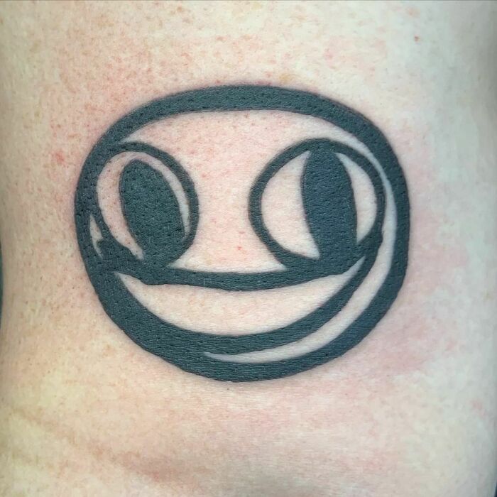 Funny tattoo of a minimalist smiley face on skin, designed in bold black lines.