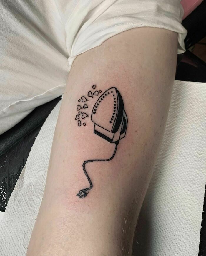 Funny tattoo of an iron with heart-shaped steam on an arm, designed to put a smile on your face.