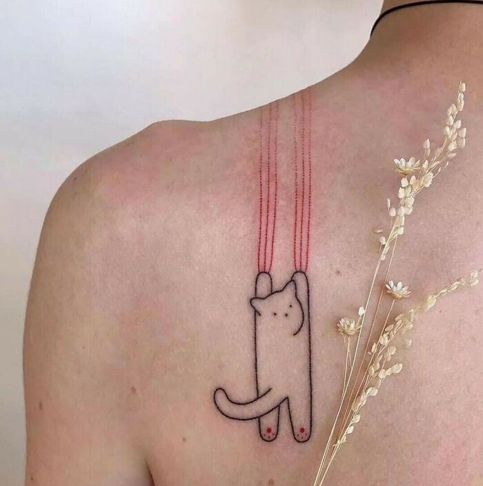 Funny tattoo of a cute cat sliding down a person's back, using red lines to create a playful effect.