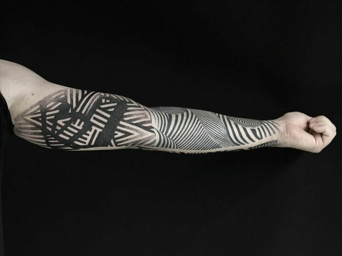 Arm with intricate optical illusion tattoo design against a black background.