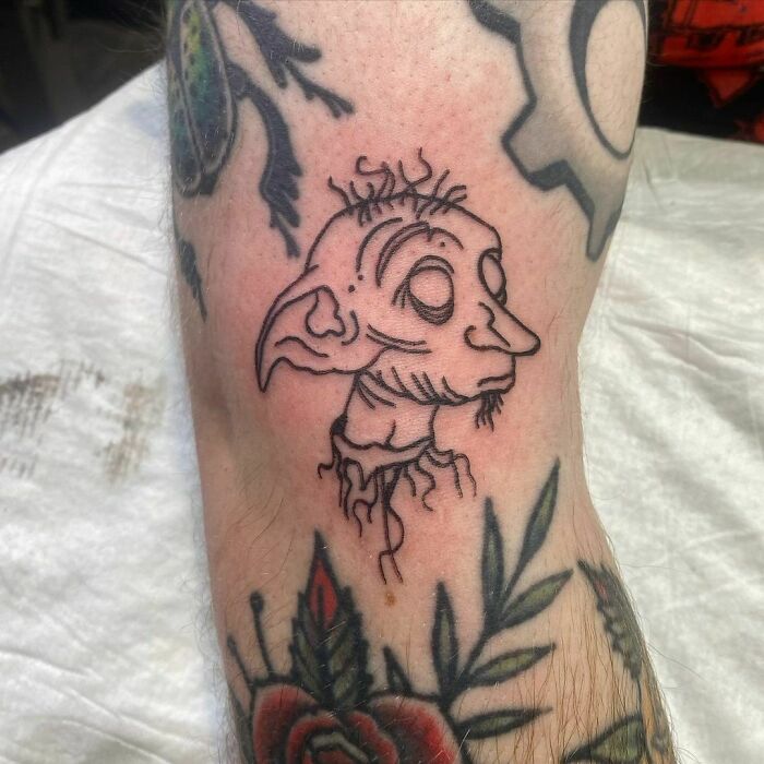 Harry Potter tattoo featuring a sketch of Dobby, inked on the forearm, surrounded by floral designs.