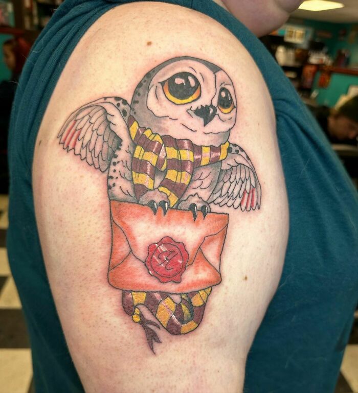 Harry Potter tattoo of an owl holding a letter, with a striped scarf, on a person's arm.