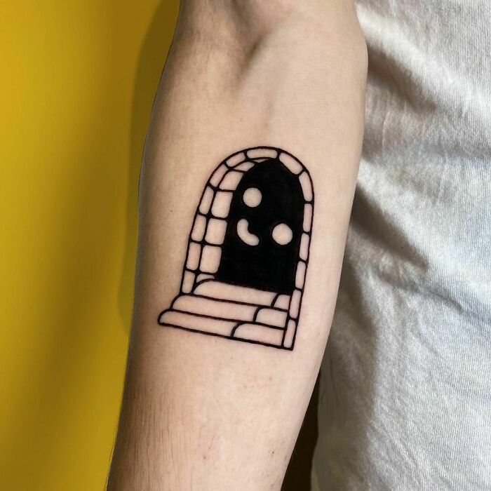 Funny tattoo of a smiling ghost in an arched brick doorway on a person's forearm.