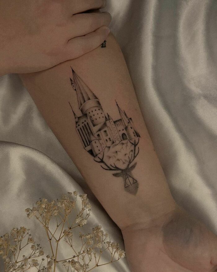 Forearm tattoo featuring Hogwarts castle with a stag and Deathly Hallows symbol; perfect for Harry Potter fans.