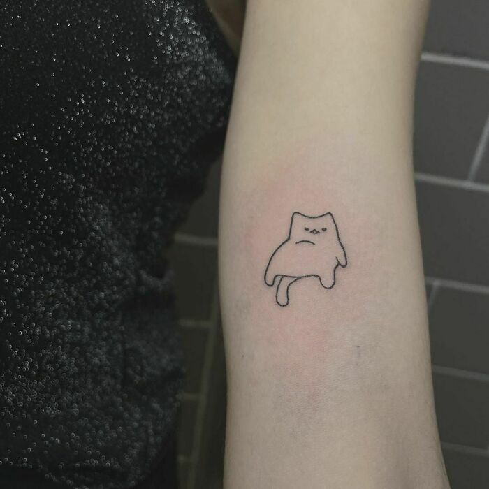 Minimalist funny tattoo of a grumpy cartoon cat on a person's arm.