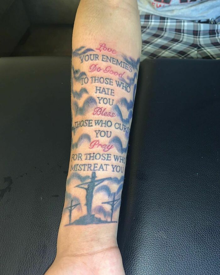 Tattoo with text about loving enemies and a silhouette, on a person's forearm.