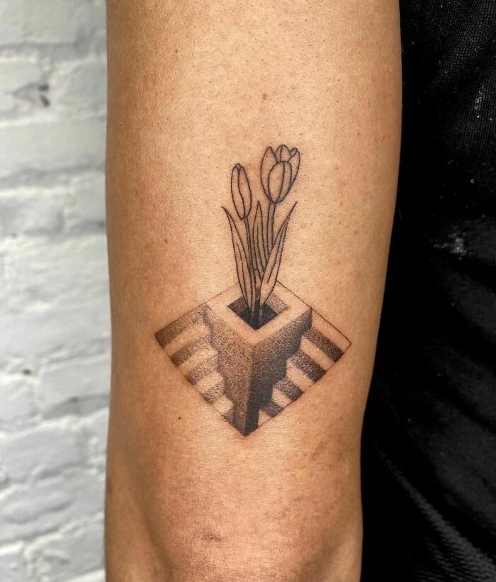 Optical illusion tattoo of tulips in a 3D box on an arm, blending realism and geometry.
