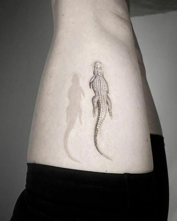Optical illusion tattoo of a realistic alligator with shadow effect on skin.