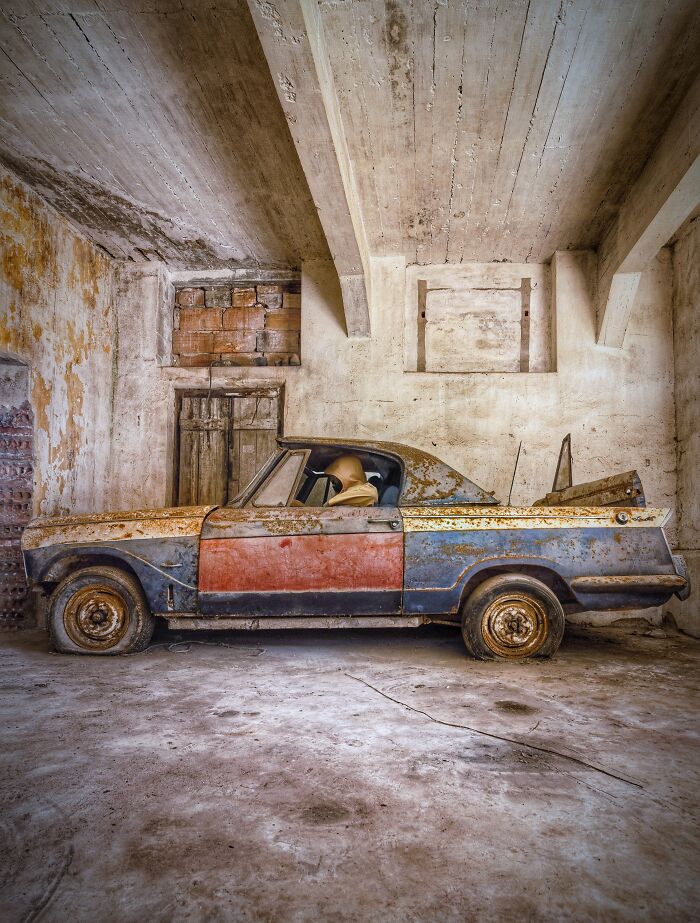 Rusty classic car abandoned inside an old factory with c*****d walls and dusty floor, showcasing urban decay and vintage automotive history.