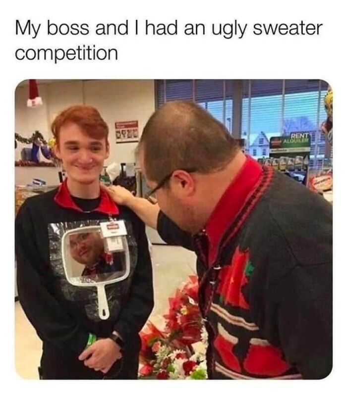 Two people at work in an ugly sweater competition, with one smiling and holding a mirror reflecting the other.