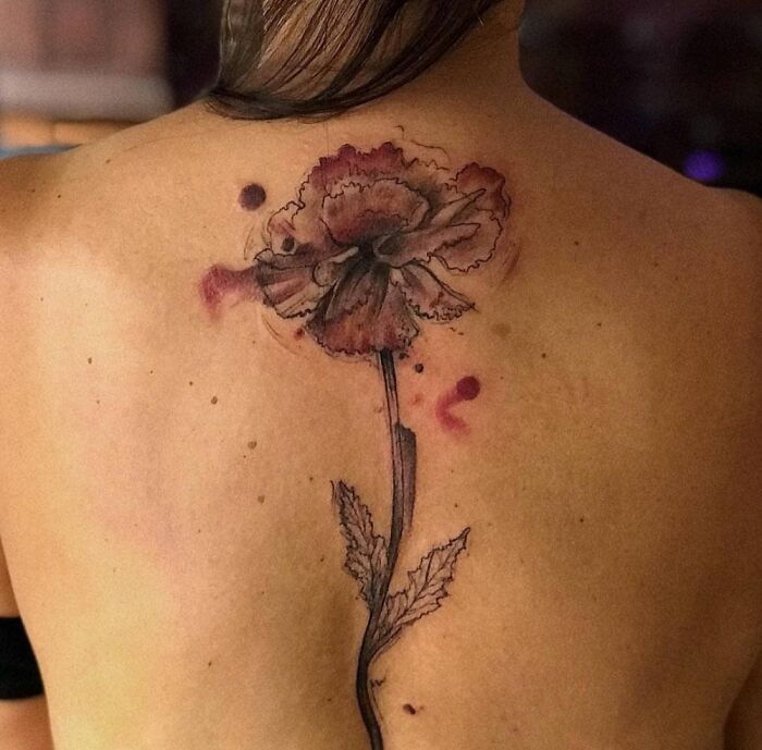 Floral tattoo on a person's back, featuring a detailed flower with watercolor effect and leaves.