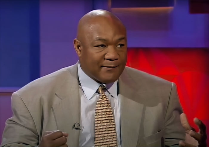 George Foreman wearing a suit and patterned tie during an interview about famous people who got married multiple times.