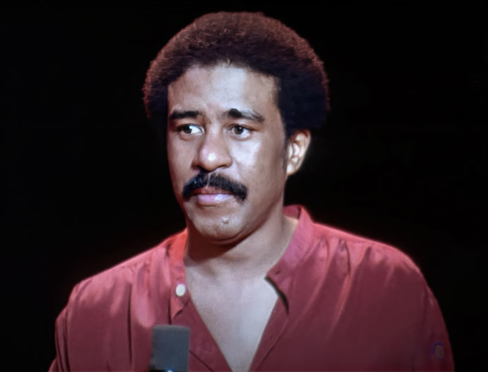 Richard Pryor wearing a red shirt, one of the famous people who got married multiple times, speaking on stage.