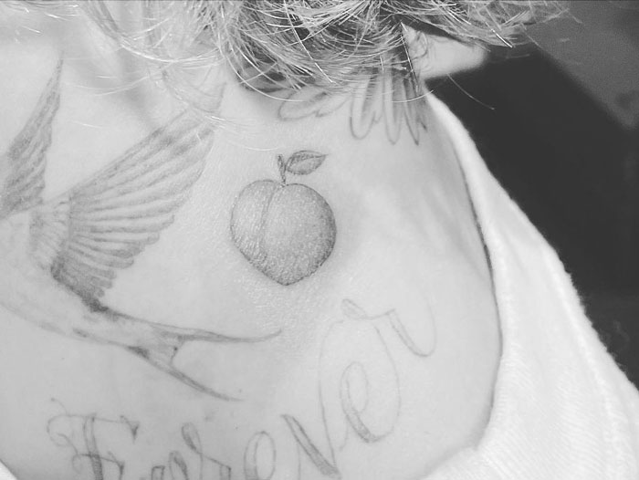 Celebrity tattoo featuring a bird and peach design with script text "forever" on skin, in black and white.