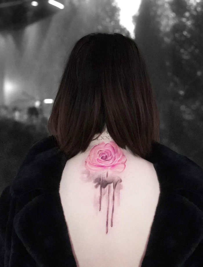 Celebrity tattoo of a pink rose on a Selena Gomez's back, seen against a blurred background.