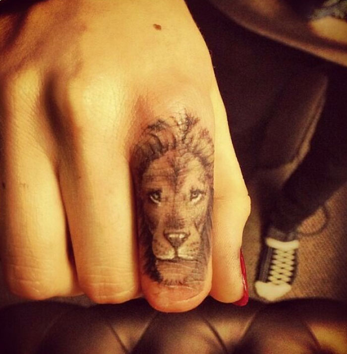 Lion tattoo on a person's finger, showing detailed artwork, inspired by celebrity tattoo designs.