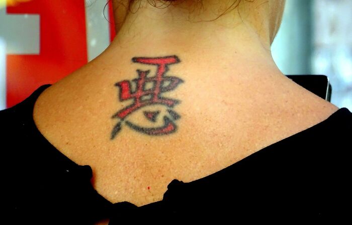 Neck tattoo with red and black Asian characters, often seen as less attractive by some people.