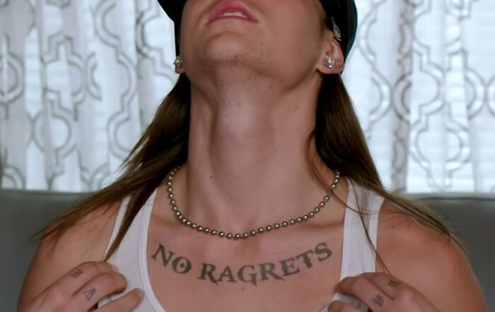 Close-up of a person with a "NO RAGRETS" tattoo on their chest, showcasing tattoo unattractiveness.